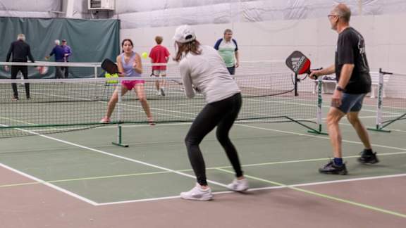 A woman in a white shirt and black pants is playing tennis with a man in a black shirt and shorts.