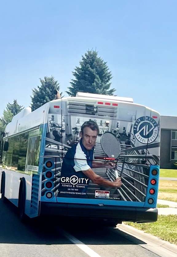 A bus with a man holding a tennis racket on the side.