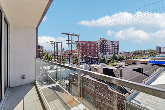A balcony with a glass railing overlooks a parking lot and buildings.