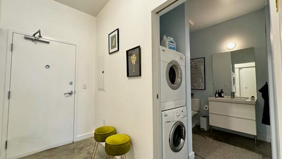 A laundry room with a washer and dryer, a mirror, and a small stool.