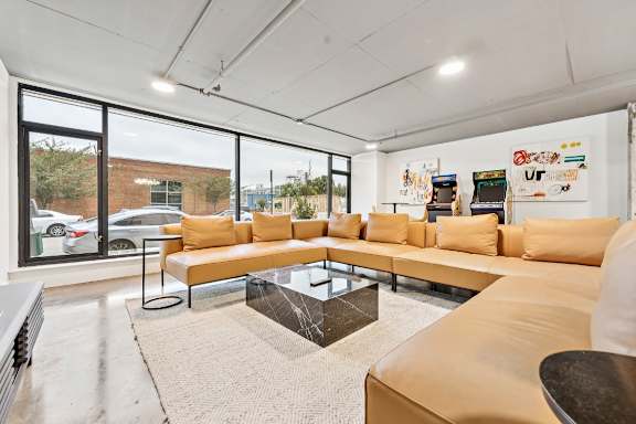 A modern living room with a large sectional sofa and a coffee table in front of a large window at The Box, Richmond, VA, 23224