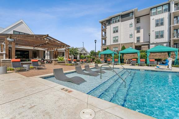 a swimming pool with lounge chairs and umbrellas next to an apartment building at Beckett Farms Apartments, PRG Real Estate Management, Fort Mill, SC