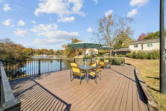 A wooden deck with yellow chairs and a table overlooking a body of water at Lakecrest Apartments, PRG Real Estate Management, Greenville, SC 29615