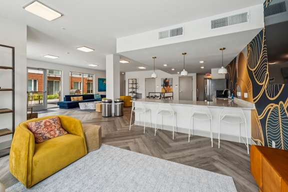 A yellow sofa with a red pillow is in the foreground of a modern living room at The Waterford At Rocketts Landing Apartments, PRG Real Estate, Richmond, VA