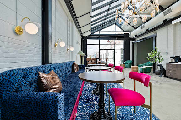 A blue patterned couch sits in a room with a glass ceiling and a table with a pink chair.