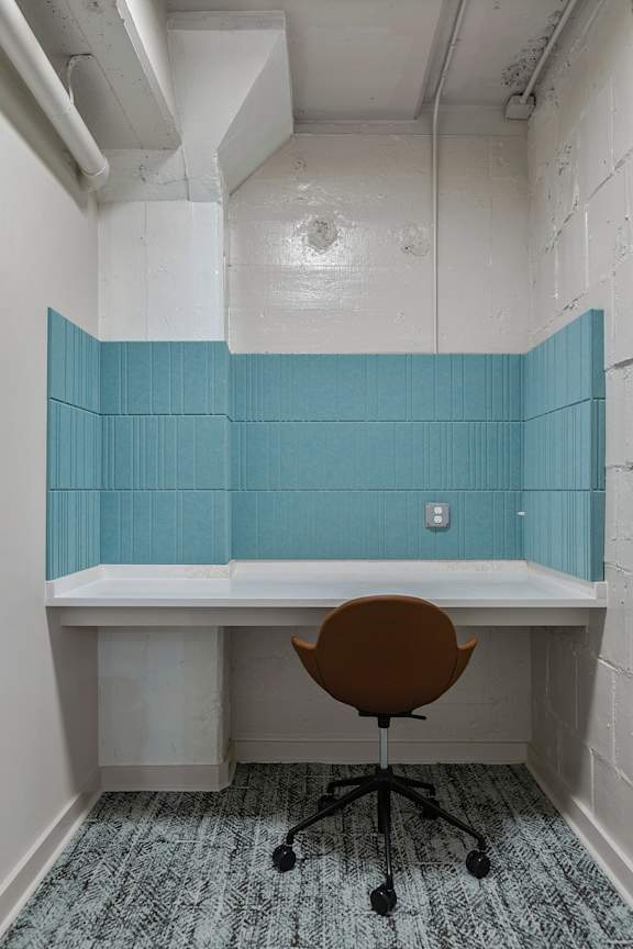 A brown chair is in front of a white desk with a blue panel on the wall.