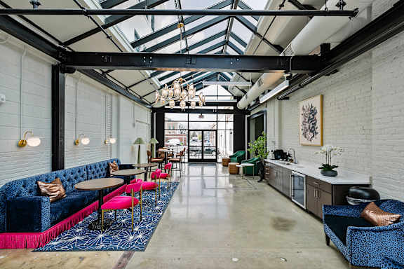 A brightly lit cafe with a blue sofa and pink chairs.