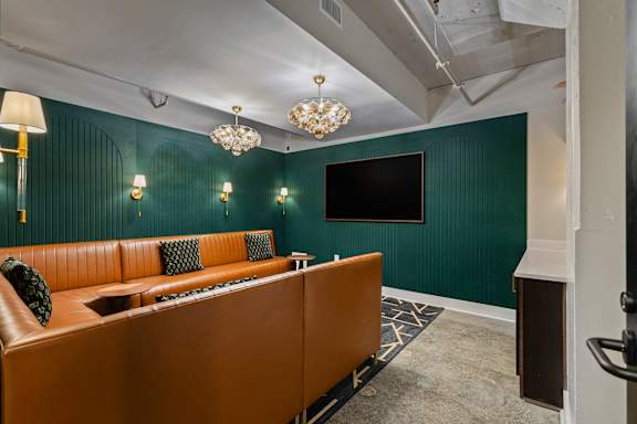 A room with a brown couch and a chandelier.