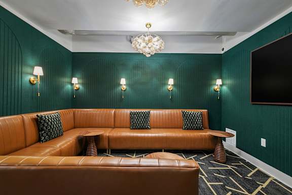 A brown leather couch with green pillows in a room with a chandelier.
