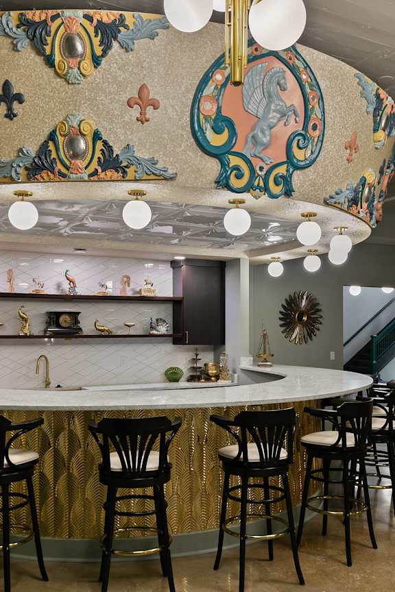 A bar with a gold and white mosaic ceiling and white bar stools.