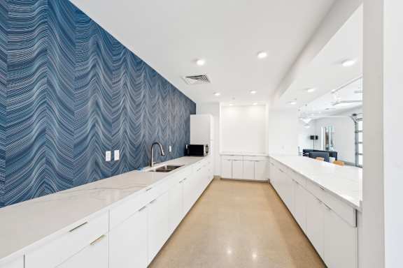 A kitchen with white cabinets and a blue patterned wallpaper.