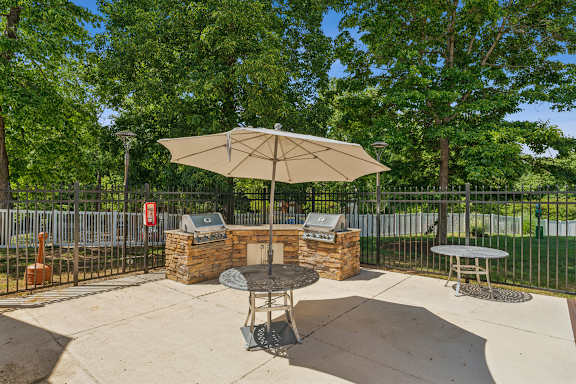 A patio with a table and chairs under an umbrella. at The Timbers Apartments, Virginia
