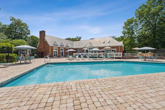 A large outdoor swimming pool with a brick patio and a house in the background at The Timbers Apartments, Richmond, VA