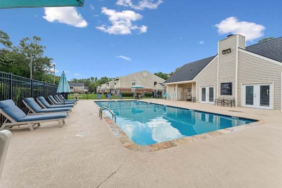 A pool with a blue umbrella and lounge chairs.