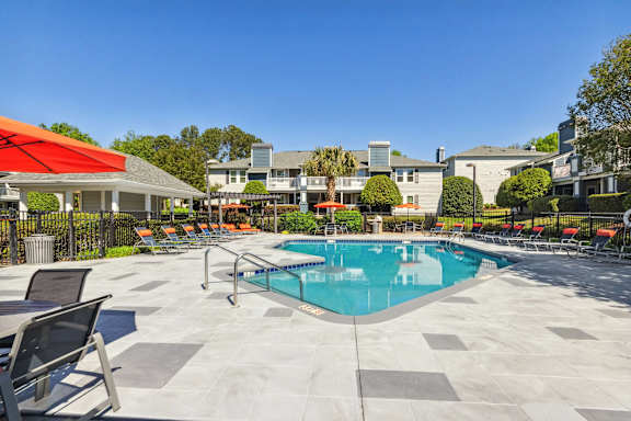 a swimming pool with chairs and umbrellas and apartments in the background at Palmetto Place Apartments, Taylors, SC, 29687