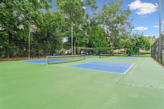 A tennis court surrounded by trees and a fence.