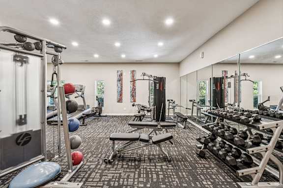 A gym with a variety of equipment including weights and a bench. at Park Ridge Estates, Durham, 27713