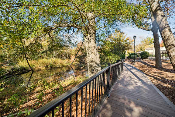 A wooden walkway with a metal railing runs through a wooded area at Lakecrest Apartments, PRG Real Estate Management, Greenville, SC 29615