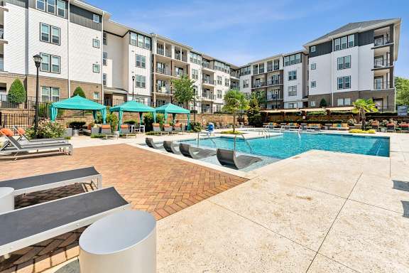 an outdoor pool with lounge chairs and umbrellas in front of an apartment building at Beckett Farms Apartments, PRG Real Estate Management, Fort Mill, SC
