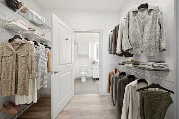 A walk in closet with clothes hanging and a toilet in the background at Circ Apartments, Virginia