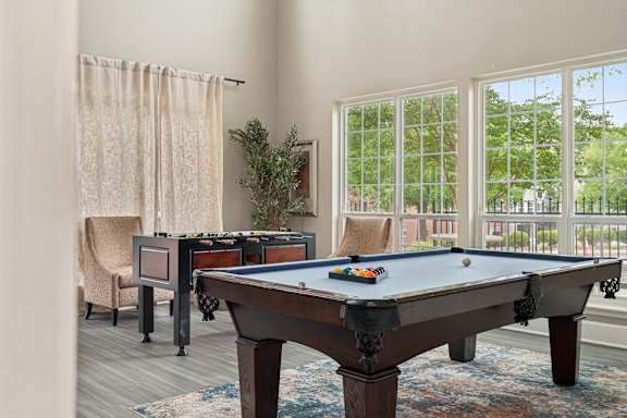 A pool table in a room with a chair and a plant.