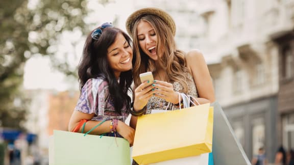 two women with shopping bags looking at a cell phone