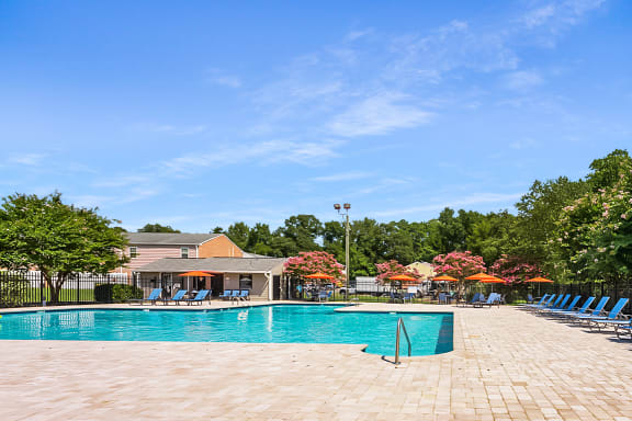 A swimming pool surrounded by trees and chairs. at Staples Mill Townhomes, Richmond, VA 23228