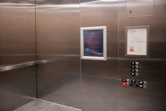 A stainless steel elevator with a control panel and a framed photo on the wall.
