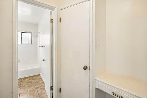 A white door with a gold handle is open to a room with a tiled floor.