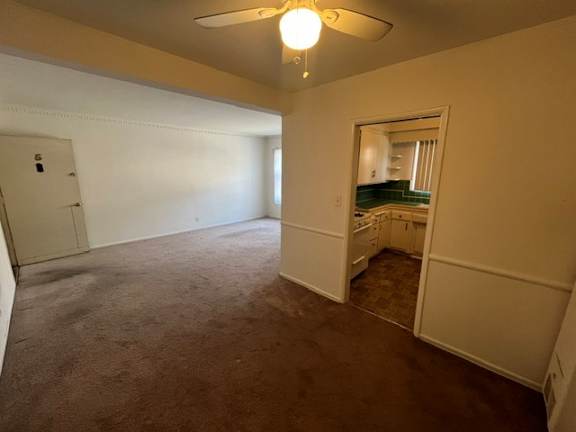 A room with a carpeted floor and a ceiling fan.