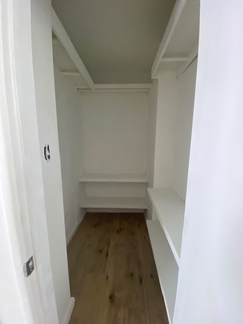 A white hallway with a wooden floor and a door on the left.