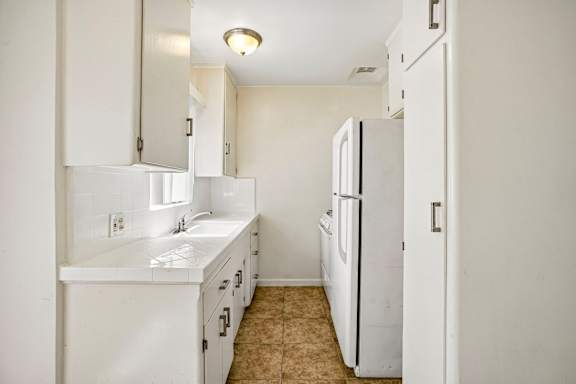 A white kitchen with a sink and a refrigerator.