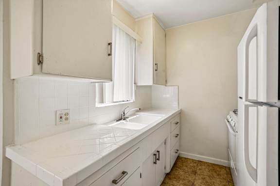 A white kitchen with a refrigerator, sink, and cabinets.