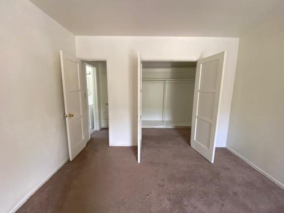 A room with carpeted floor and white walls with a doorway open to another room.