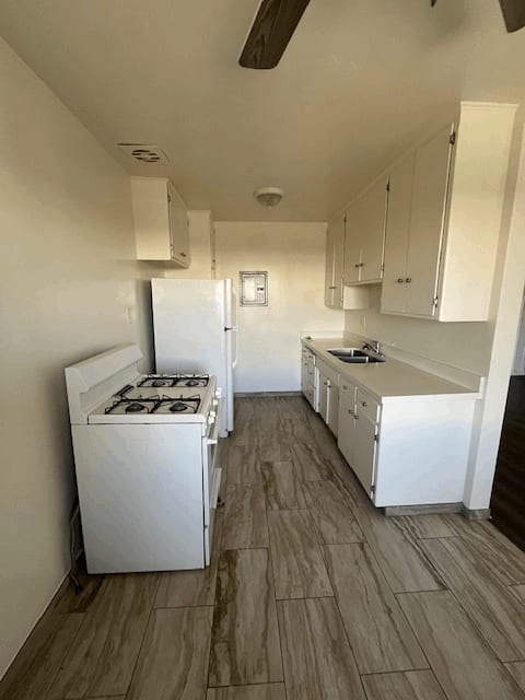 A white kitchen with a wood floor and white appliances.