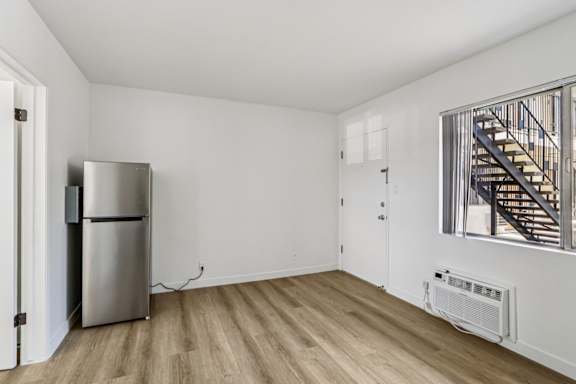 A room with a stainless steel refrigerator and a wooden floor.