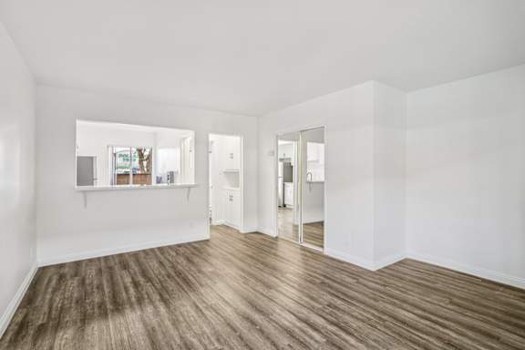 A room with white walls and wooden flooring with a shelf and a mirror.