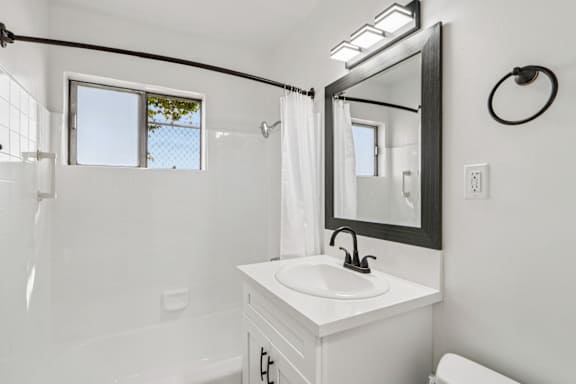 A white bathroom with a sink, mirror, and tub.