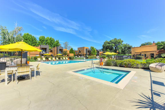Community Spa on a sunny day with blue skies. There are tables with umbrellas nearby.at Fountains of Fair Oaks, Fair Oaks, 95628