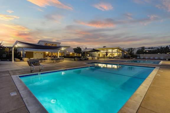 A large swimming pool in front of a building with a sunset in the background.
