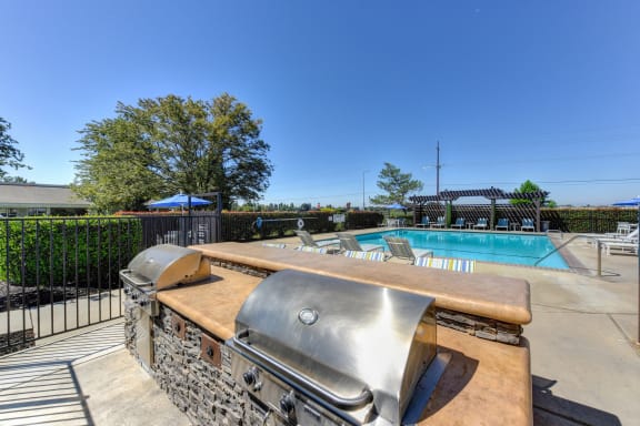 BBQ Picnic Area with Grills and View of Lounge Chairs and Pool  at Silverstone Apartments, Davis