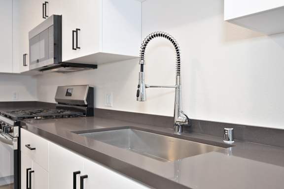 A modern kitchen with a stainless steel sink and a black microwave above the stove.