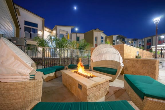 A patio with a fire pit and seating area at night.
