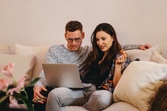 Couple on couch viewing an open laptop together. at Silverstone Apartments, Davis ,95618