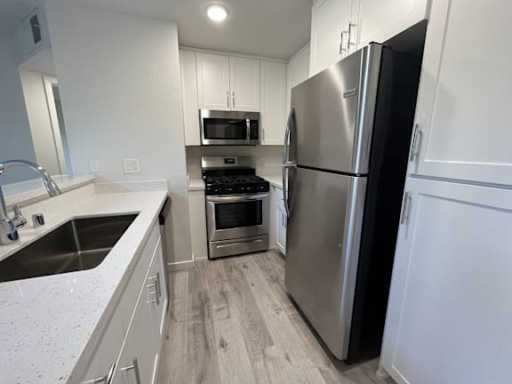 A kitchen with a refrigerator, sink, oven, and microwave.