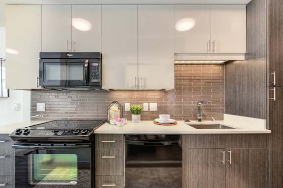 A modern kitchen with a black stove top oven and a black microwave above a white counter at Rivet Apartments, Washington 98109
