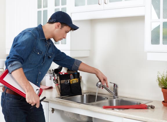 Maintenance employee working on a repair on the kitchen sink.  He has a clipboard in hand and tool bag on the counter. at Silverstone Apartments, Davis, CA