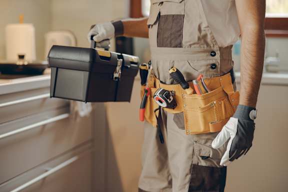 A man in a tool belt holding a toolbox.