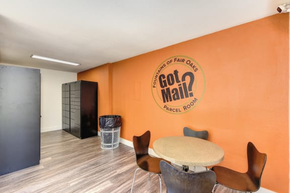 Parcel Room with Hardwood Inspired Floor, Short Round Tables, Chairs, Orange Wall with at Fountains of Fair Oaks, Fair Oaks