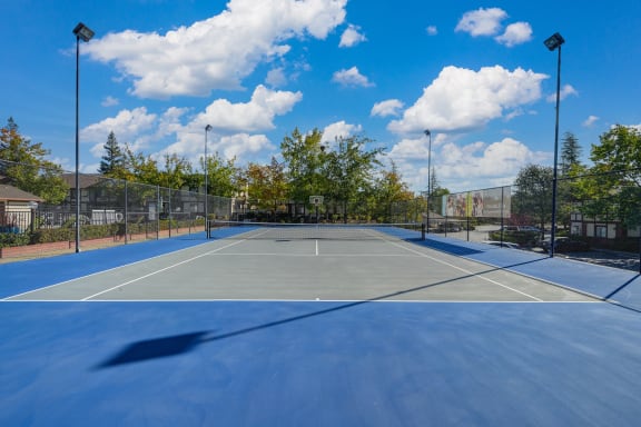 a tennis court with trees and a blue sky with clouds at Rocklin Manor  Apartments, California, 95677